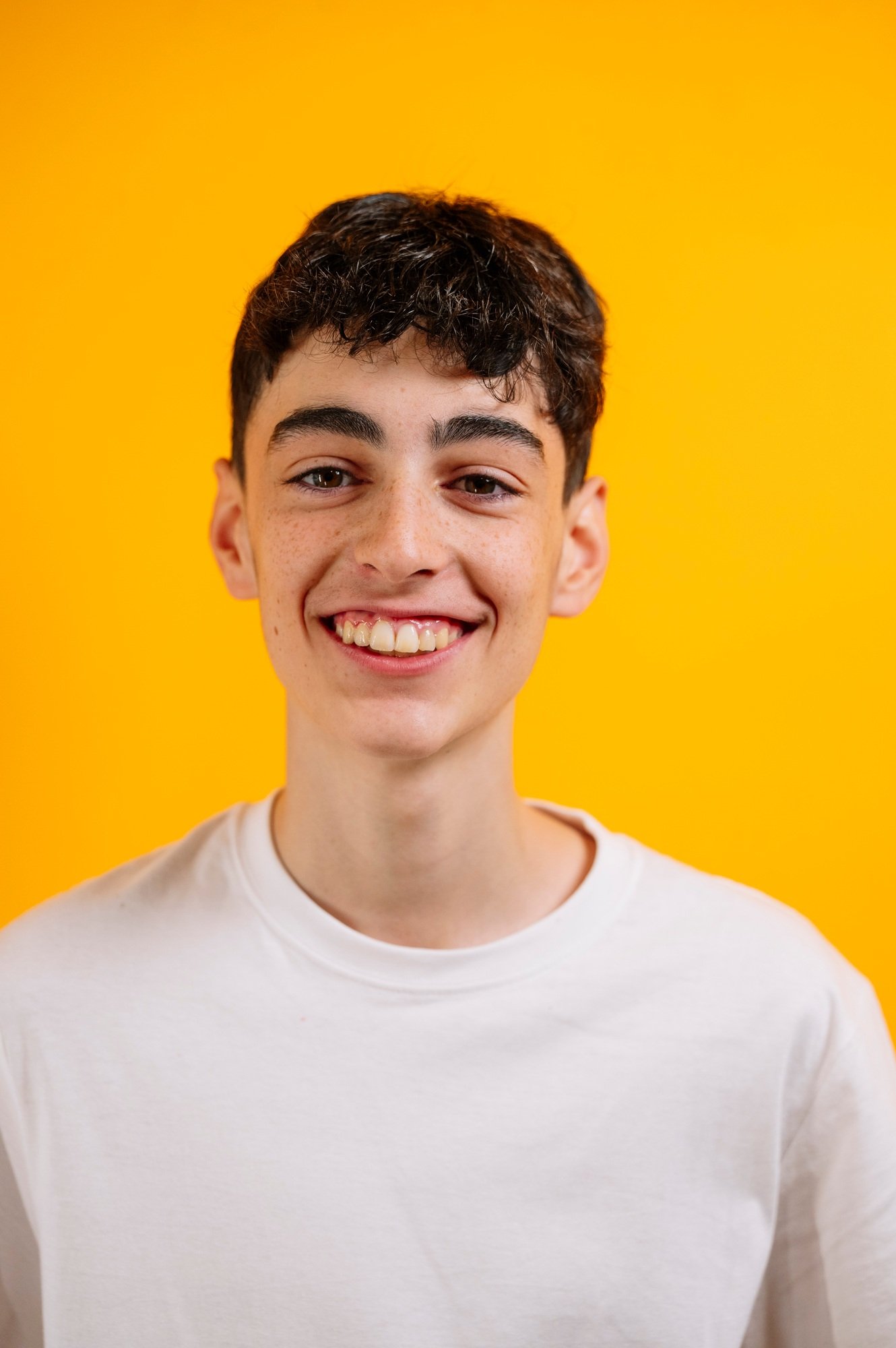 Smiling teen boy in white t-shirt, yellow background.